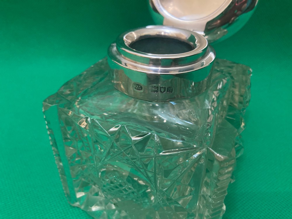 A square clear cut glass inkwell with a diamond facet pattern and a polished silver hinged domed cap. View III