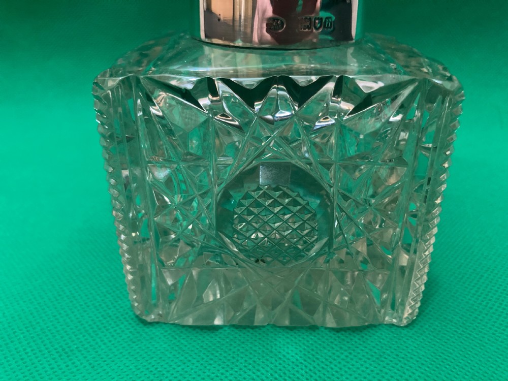 A square clear cut glass inkwell with a diamond facet pattern and a polished silver hinged domed cap. View IV