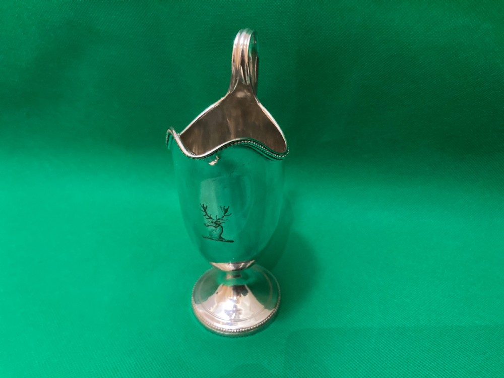 A polished silver helmet-shaped cream jug featuring a beaded rim, a high looped handle, and a round pedestal foot. View II