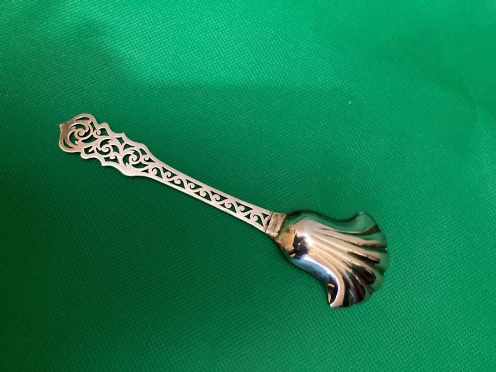 An antique silver sugar caddy spoon featuring a fluted shell-shaped bowl with British hallmarks and an openwork pierced scroll handle. View III