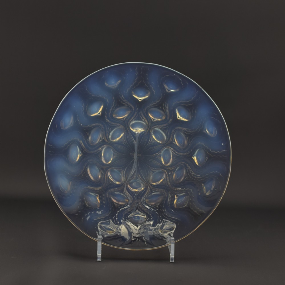 A circular Art Deco opalescent glass plate featuring a repeating pattern of raised oval bulbous motifs emitting a milky blue hue.