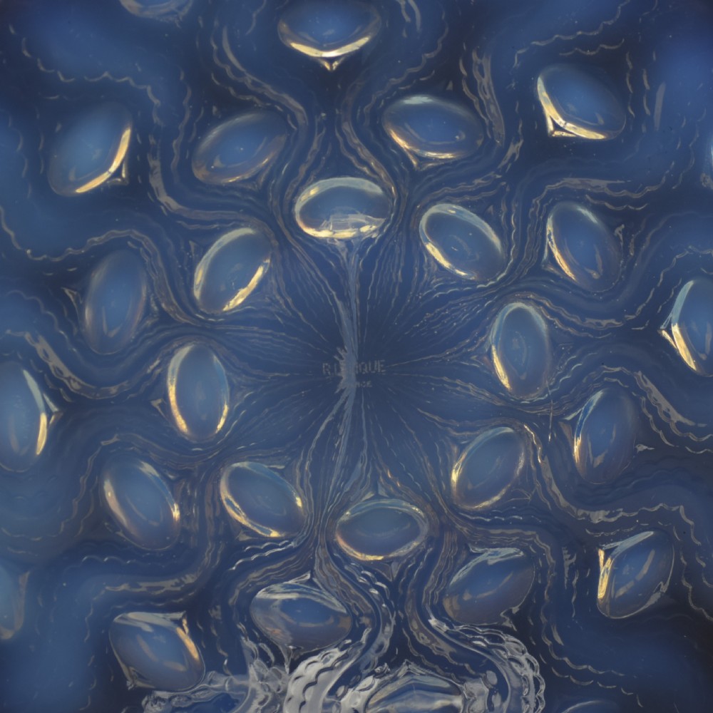 A circular Art Deco opalescent glass plate featuring a repeating pattern of raised oval bulbous motifs emitting a milky blue hue. View VI