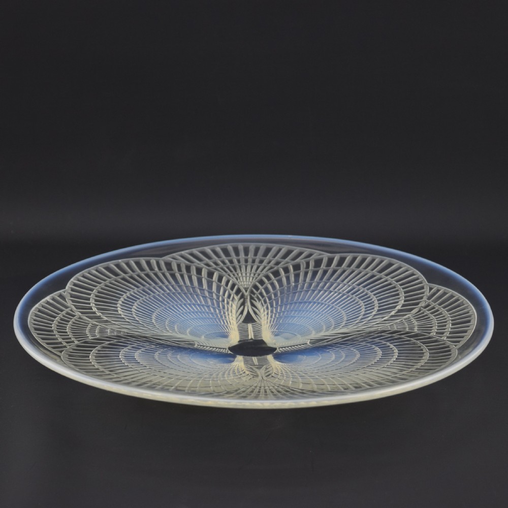 A circular Art Deco opalescent glass plate featuring a relief-moulded four-shell Coquilles design with milky blue tones. View VI