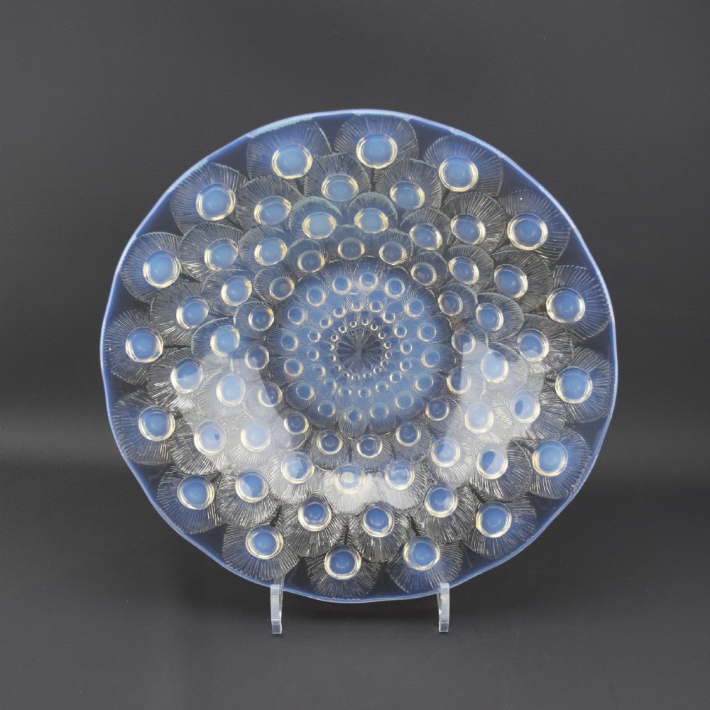 A circular Art Deco opalescent blue glass coupe dish moulded with concentric peacock feather motifs featuring prominent circular cabochons.