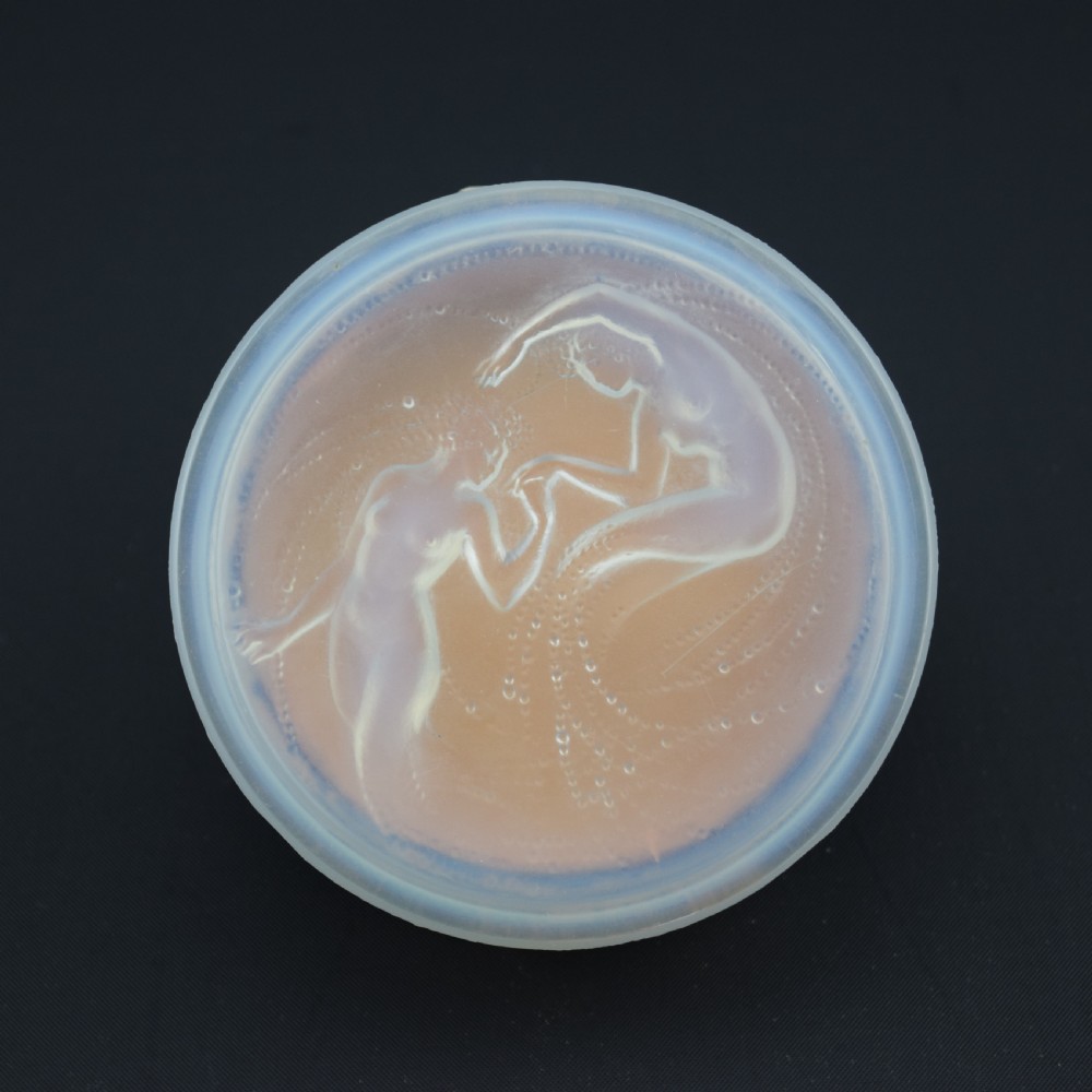 A circular translucent opalescent glass box lid featuring a high-relief moulded depiction of two figures amidst swirling water bubbles.