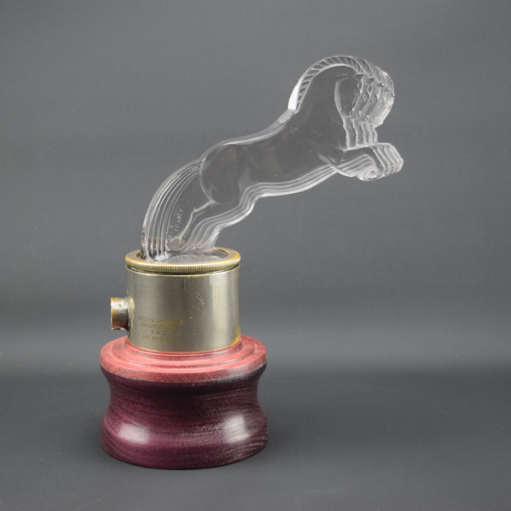 An Art Deco clear moulded glass car mascot depicting five galloping horses in profile, mounted on a cylindrical metal collar and turned wood base.