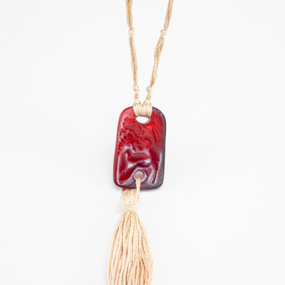 A rectangular Rene Lalique red moulded glass pendant depicting a child holding two doves, suspended from a beige woven cord with a matching lower tassel.