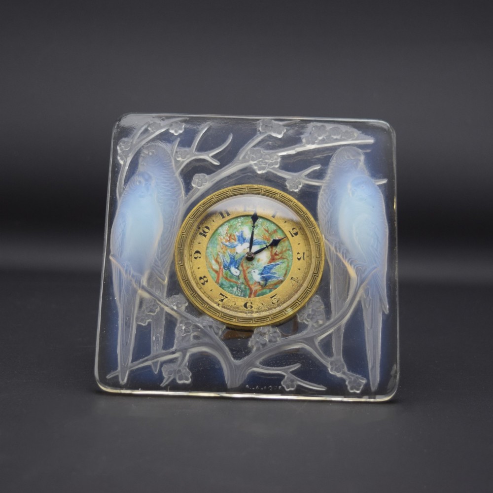 A square Rene Lalique Art Deco opalescent glass clock depicting moulded lovebirds amongst branches around a central circular brass dial.
