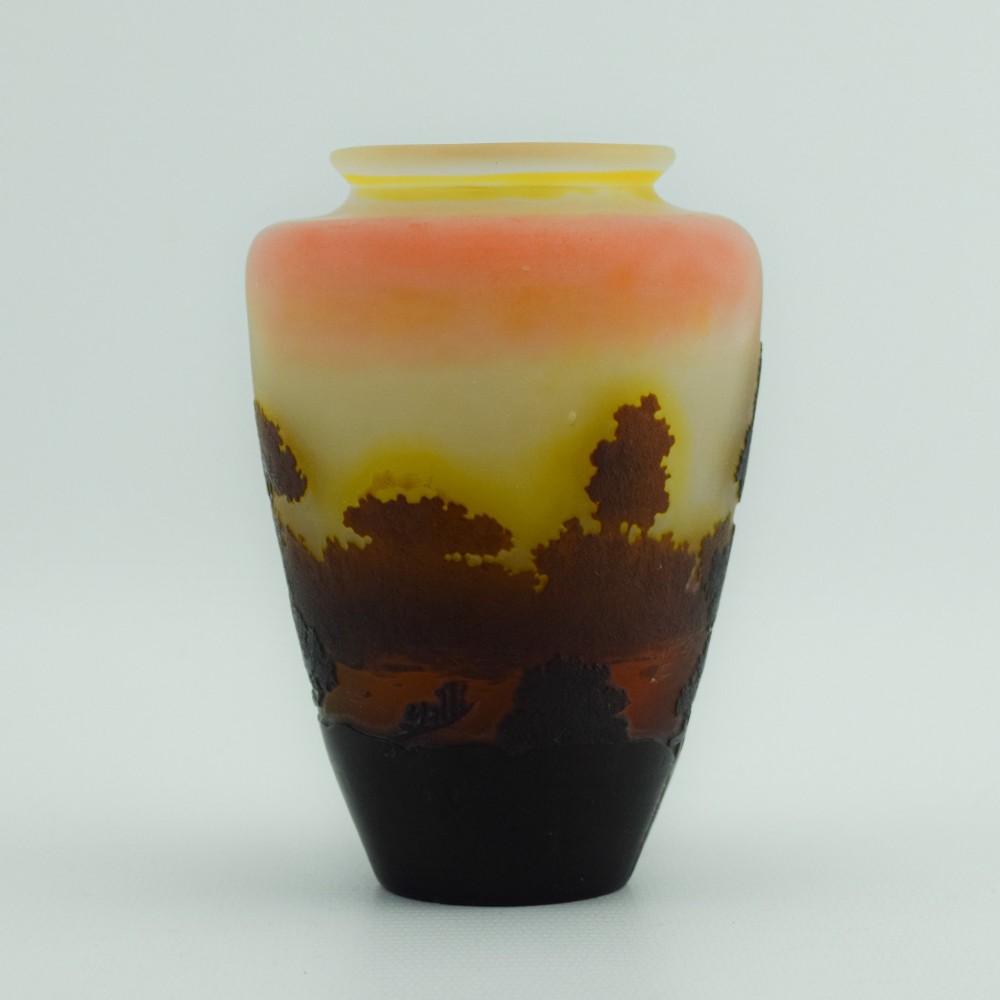 An Art Nouveau cameo glass vase featuring an acid-etched dark brown woodland landscape set against a warm yellow and soft pink background. View VI