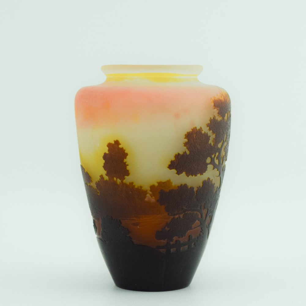 An Art Nouveau cameo glass vase featuring an acid-etched dark brown woodland landscape set against a warm yellow and soft pink background. View VII