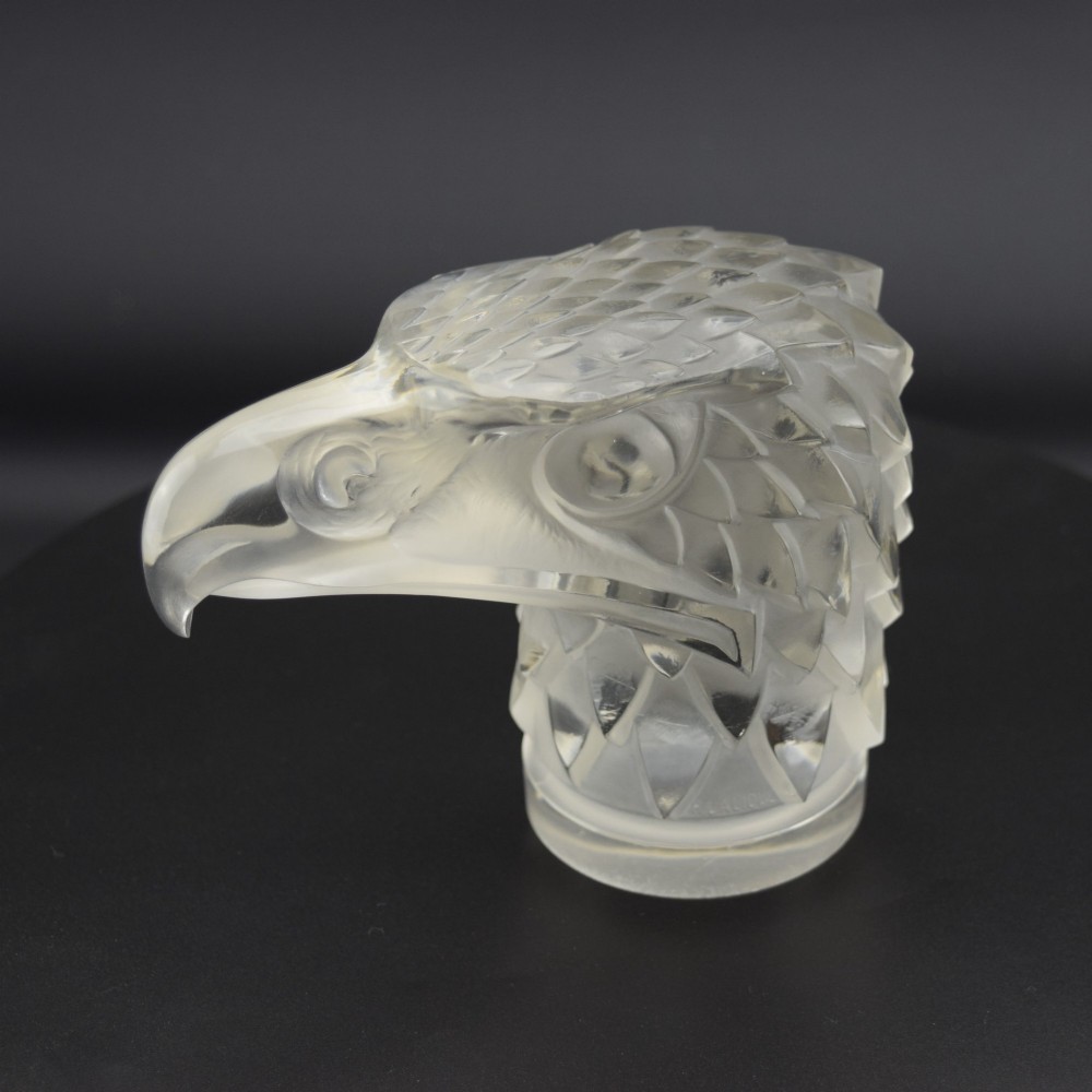 A clear and frosted moulded glass sculpture depicting an eagle head in profile, designed as an Art Deco automobile mascot. View VI