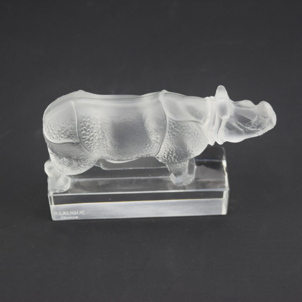 A moulded clear and frosted glass paperweight featuring a stylized rhinoceros standing on an integral rectangular base, marked R. Lalique France. View VII