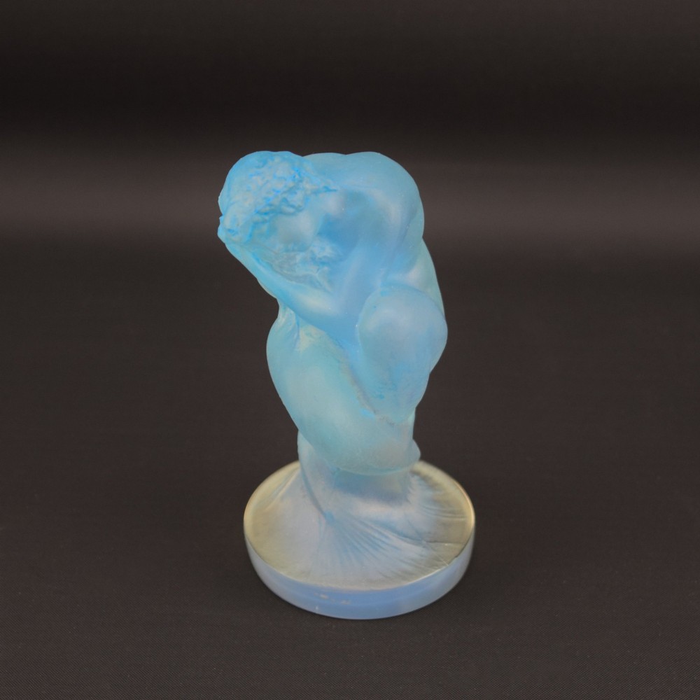 An Art Deco opalescent blue glass car mascot depicting a Sirene or mermaid-like crouching figure on a circular base. View VI