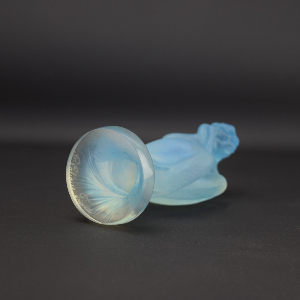 An Art Deco opalescent blue glass car mascot depicting a Sirene or mermaid-like crouching figure on a circular base. View VII