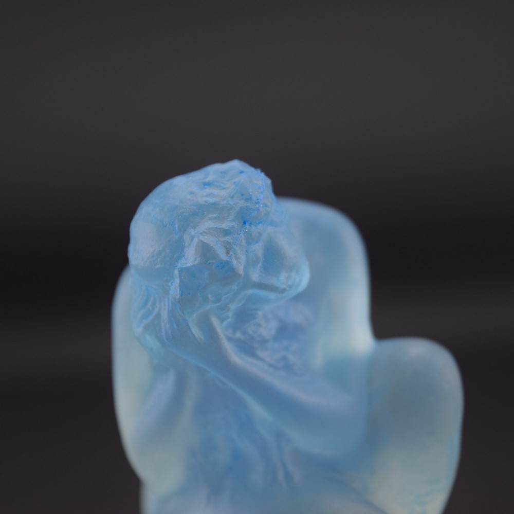 An Art Deco opalescent blue glass car mascot depicting a Sirene or mermaid-like crouching figure on a circular base. View XI