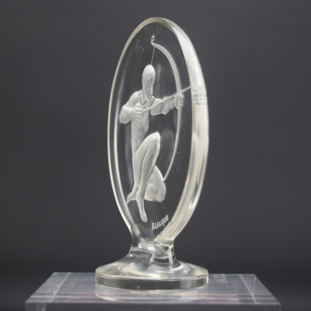 A circular clear and frosted Art Deco glass car mascot by Rene Lalique featuring a relief carving of a kneeling archer drawing a bow. View II