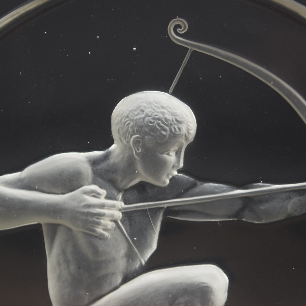 A circular clear and frosted Art Deco glass car mascot by Rene Lalique featuring a relief carving of a kneeling archer drawing a bow. View VIII