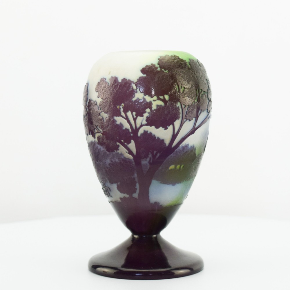 An Art Nouveau cameo glass footed vase depicting a dark purple tree landscape against a frosted green and white background.
