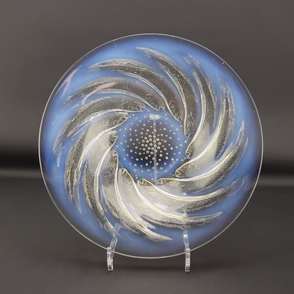 A circular Art Deco opalescent blue glass shallow bowl decorated with a spiralling pattern of moulded fish and a central field of small raised bubbles.