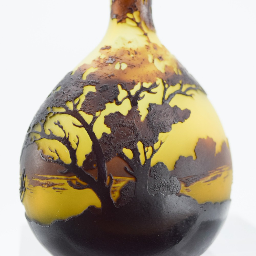 A yellow and dark brown Art Nouveau cameo glass vase featuring an acid-etched forest landscape with trees and birds on a long slender neck. View IX