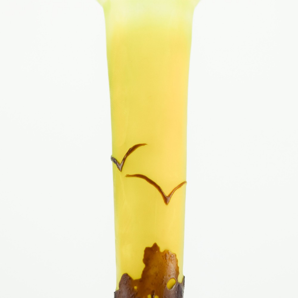A yellow and dark brown Art Nouveau cameo glass vase featuring an acid-etched forest landscape with trees and birds on a long slender neck. View X