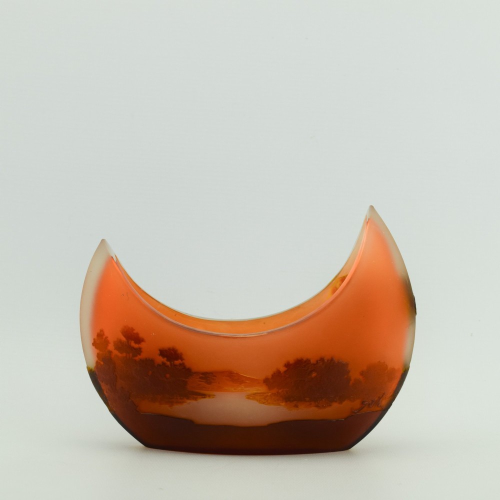 A crescent-shaped Art Nouveau cameo glass vase featuring an acid-etched river landscape in shades of burnt orange and dark brown against a frosted background.