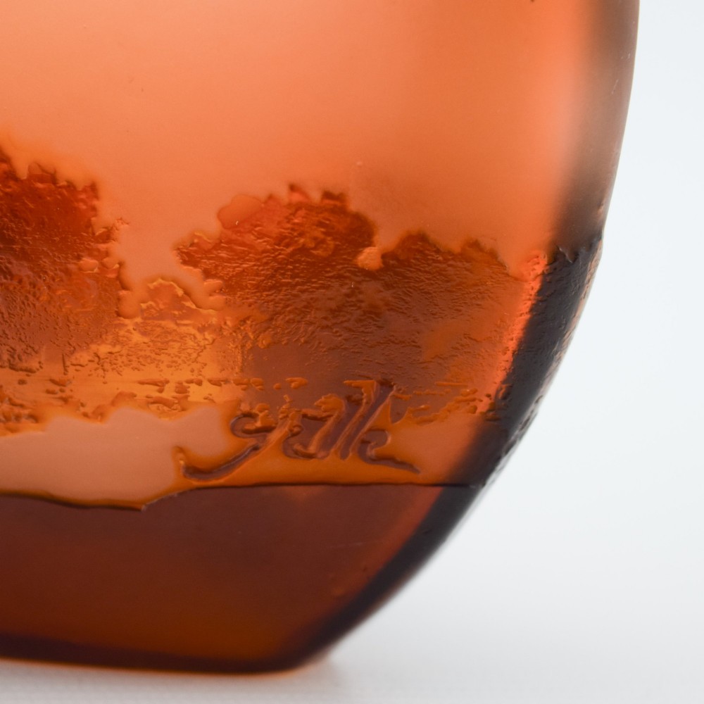 A crescent-shaped Art Nouveau cameo glass vase featuring an acid-etched river landscape in shades of burnt orange and dark brown against a frosted background. View X