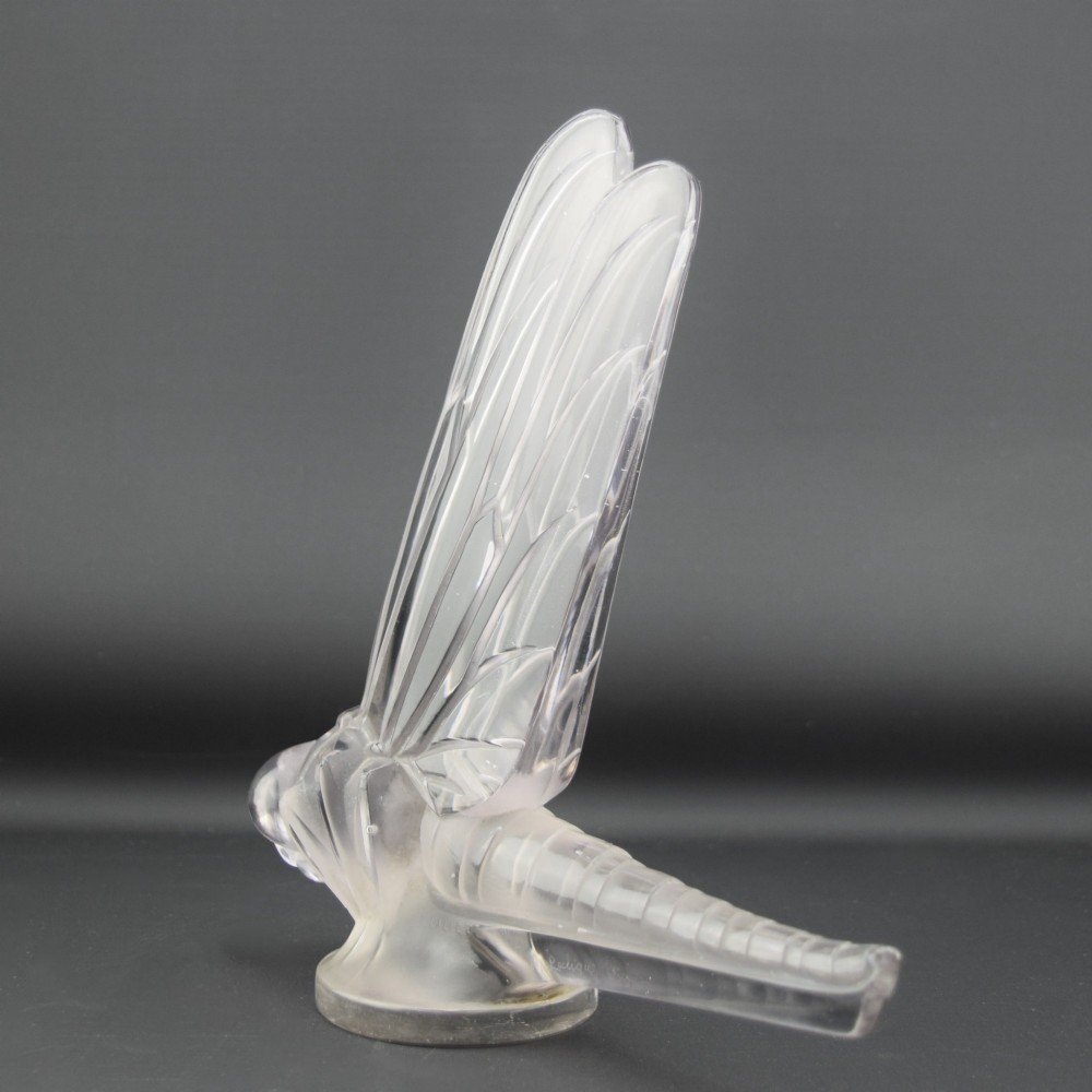 An Art Deco clear and frosted glass car mascot sculpted in the form of a stylised dragonfly with upright wings resting on a circular base. View V