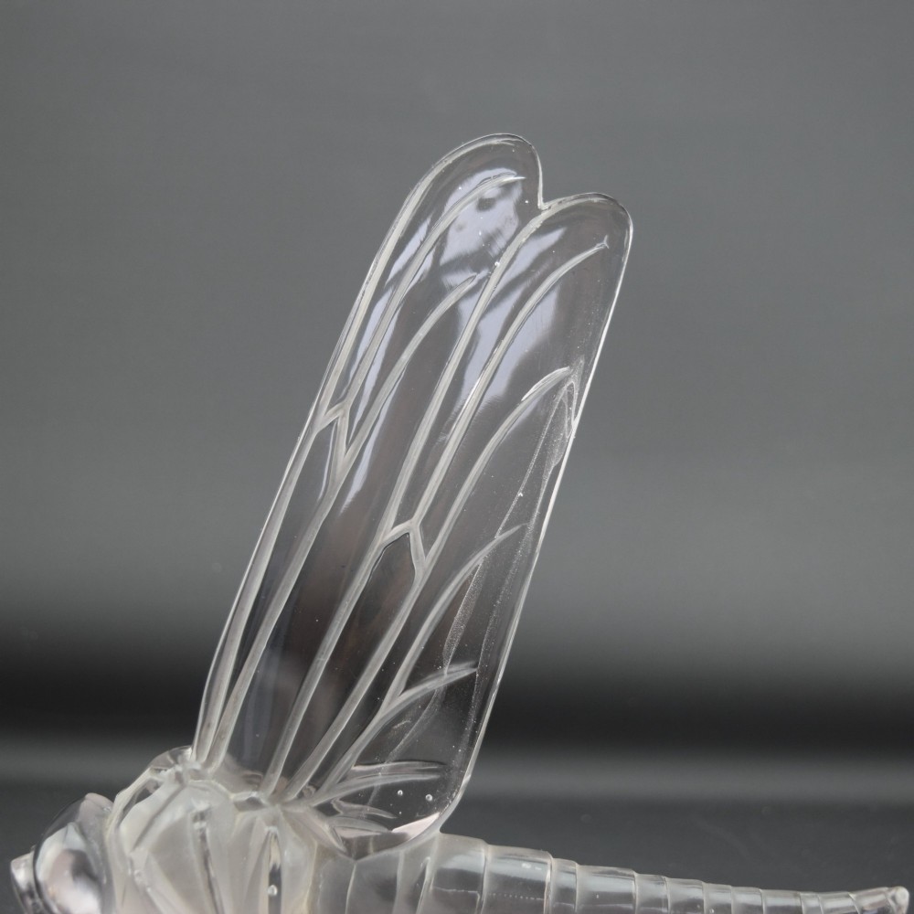 An Art Deco clear and frosted glass car mascot sculpted in the form of a stylised dragonfly with upright wings resting on a circular base. View VII
