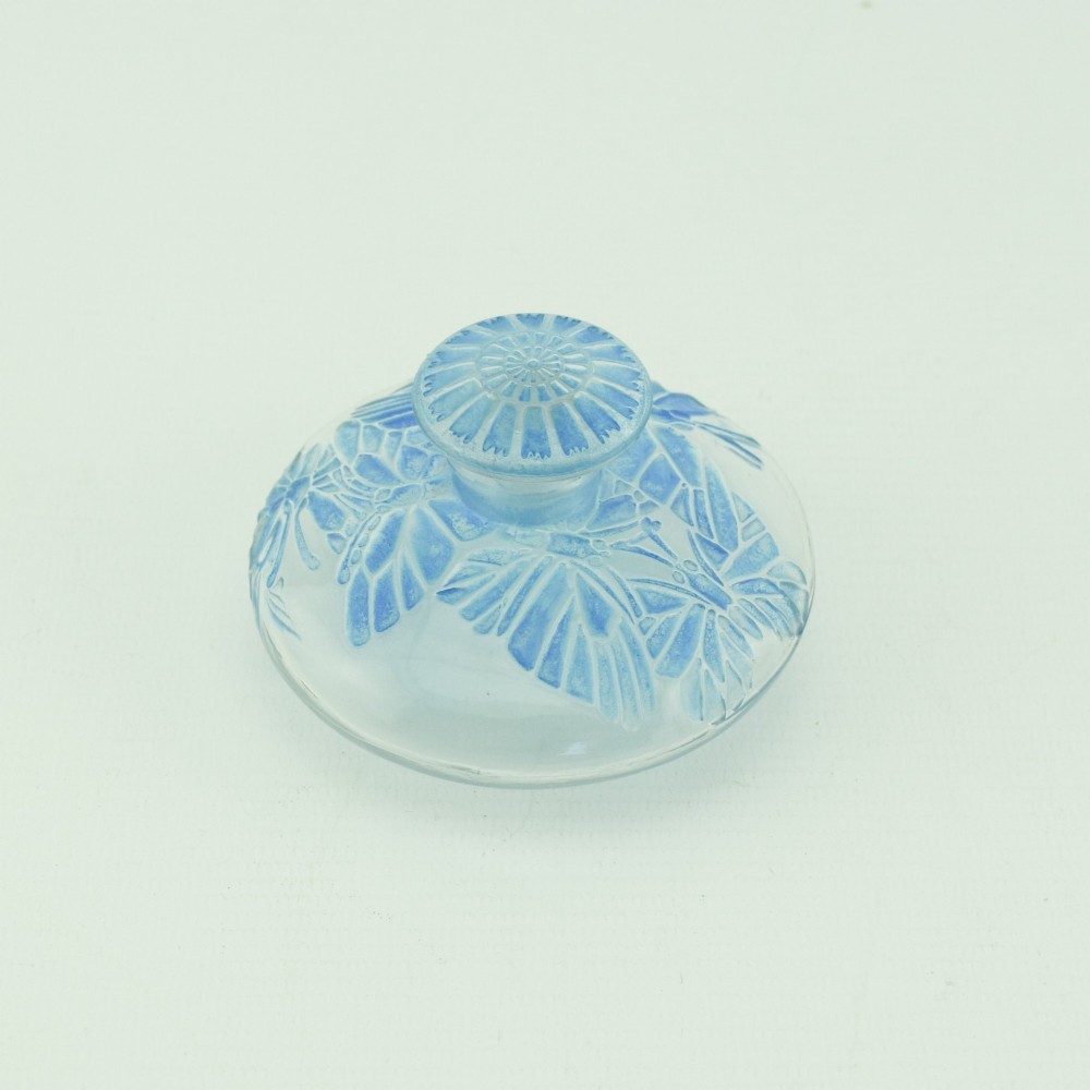 A circular Art Deco clear glass perfume bottle featuring relief butterfly motifs stained in blue with a matching circular glass stopper. View II