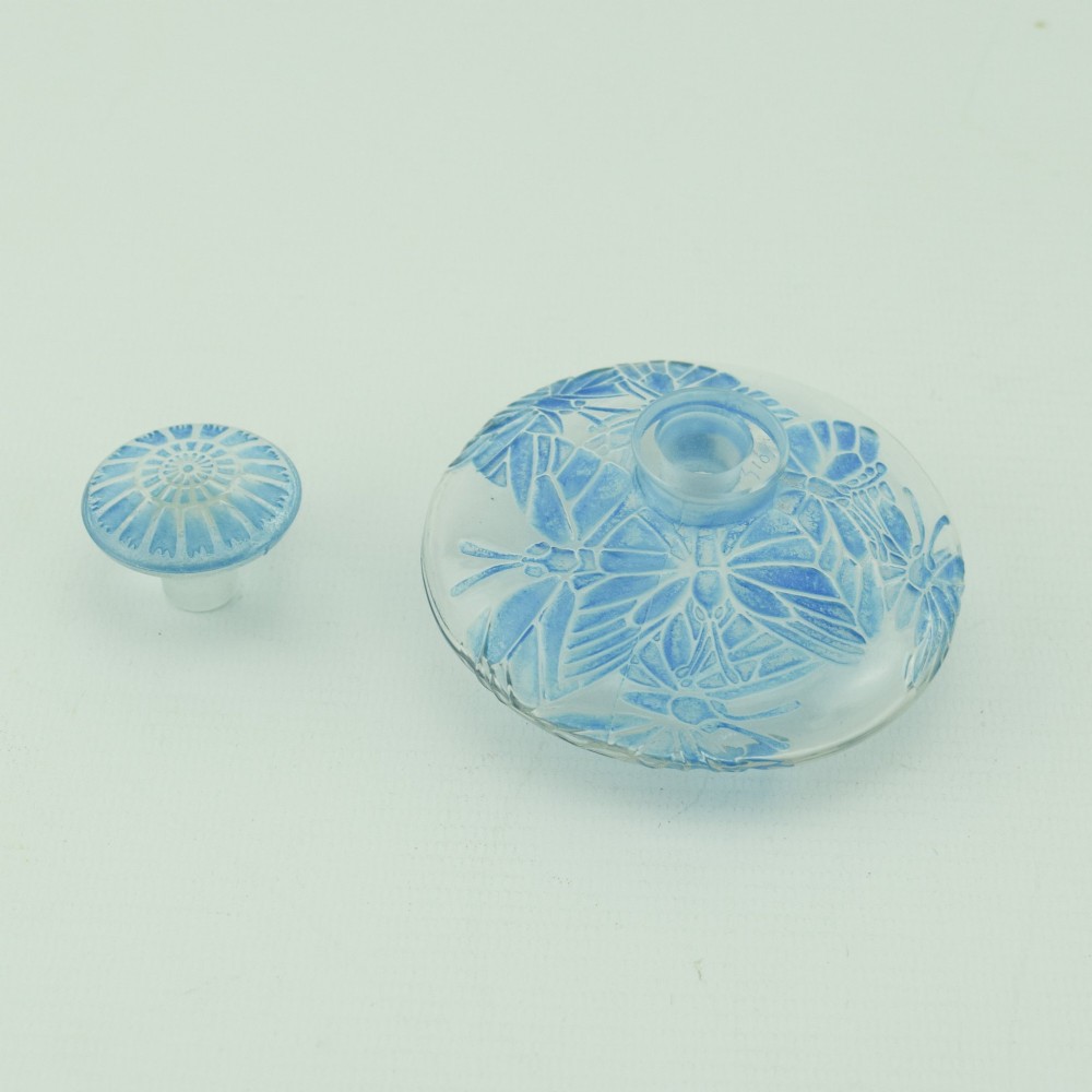 A circular Art Deco clear glass perfume bottle featuring relief butterfly motifs stained in blue with a matching circular glass stopper. View V