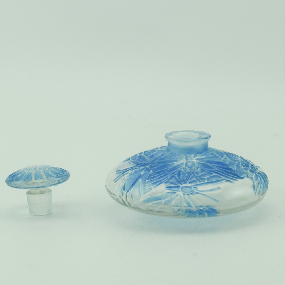 A circular Art Deco clear glass perfume bottle featuring relief butterfly motifs stained in blue with a matching circular glass stopper. View VI