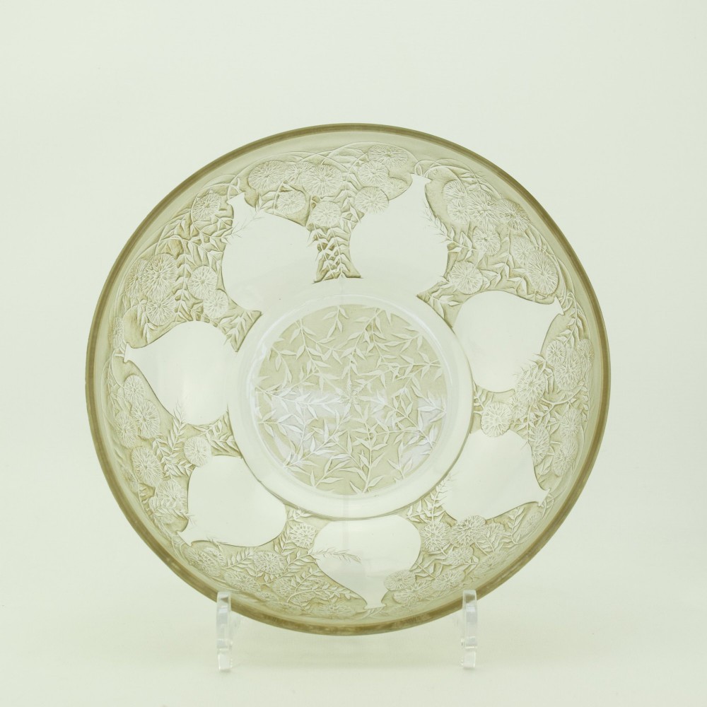 A circular clear glass shallow coupe bowl featuring frosted relief patterns of small vases and botanical motifs around a central medallion.