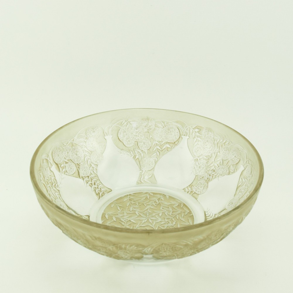 A circular clear glass shallow coupe bowl featuring frosted relief patterns of small vases and botanical motifs around a central medallion. View V
