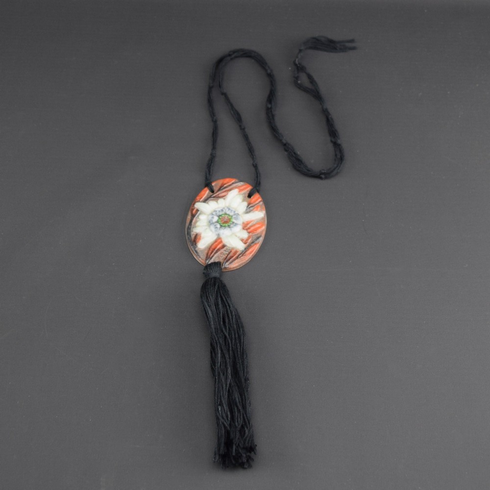 An oval Art Deco pate-de-verre glass pendant featuring a white floral sea thistle motif surrounded by orange accents, suspended from a black cord with a lower thread tassel. View III
