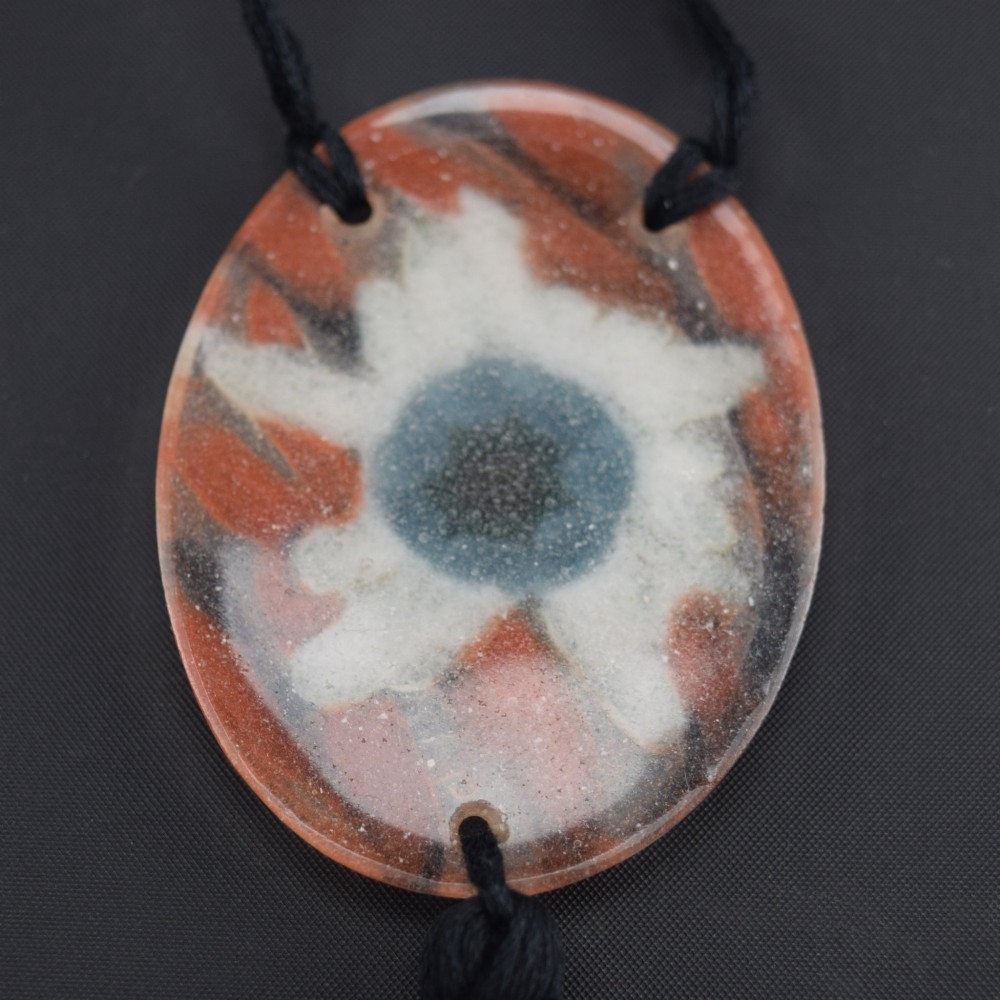 An oval Art Deco pate-de-verre glass pendant featuring a white floral sea thistle motif surrounded by orange accents, suspended from a black cord with a lower thread tassel. View VI