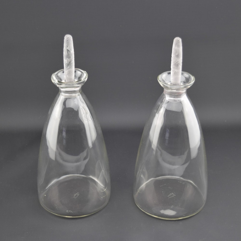 A pair of clear glass Art Deco conical decanters featuring elongated frosted glass stoppers with delicate leaf motifs. View II