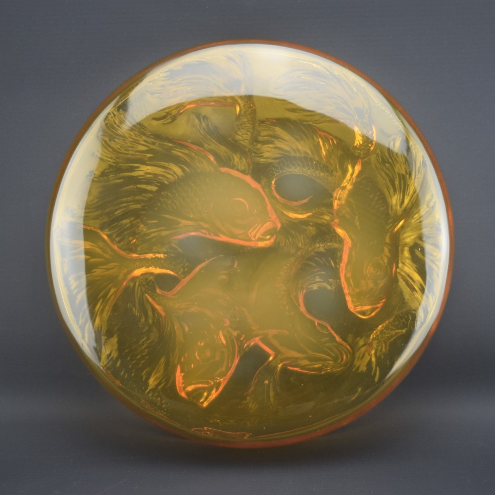 A circular amber opalescent glass box decorated with relief-moulded carp fish swirling in a central motif.