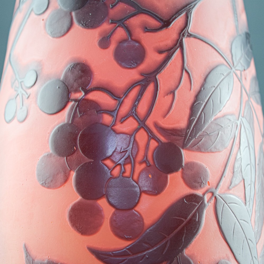 An Art Nouveau tapered cameo glass vase featuring a frosted coral orange ground with acid-etched dark red botanical leaf and berry motifs. View X