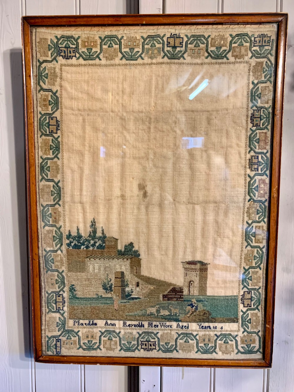 A framed early nineteenth-century needlework sampler featuring an embroidered architectural scene and floral border on a natural linen ground. View II