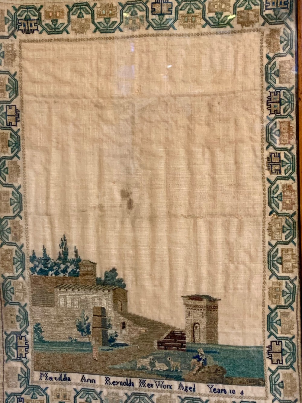 A framed early nineteenth-century needlework sampler featuring an embroidered architectural scene and floral border on a natural linen ground. View IV