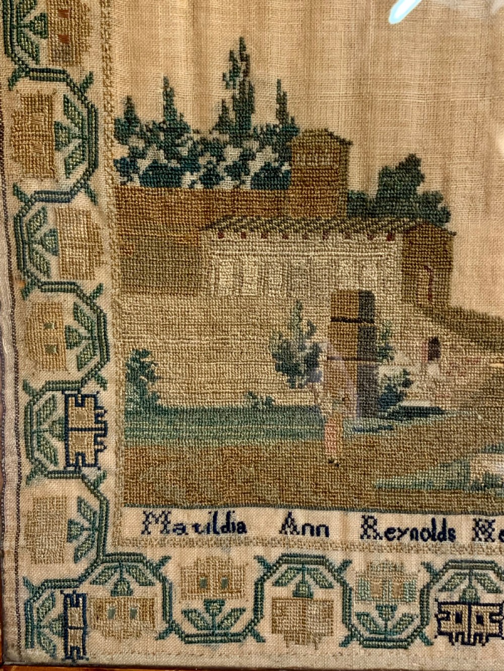 A framed early nineteenth-century needlework sampler featuring an embroidered architectural scene and floral border on a natural linen ground. View VI