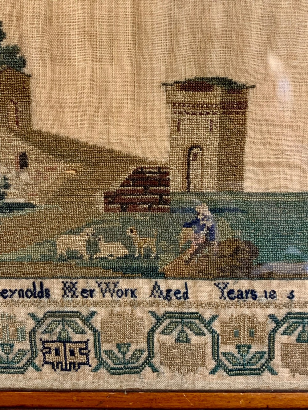 A framed early nineteenth-century needlework sampler featuring an embroidered architectural scene and floral border on a natural linen ground. View VII