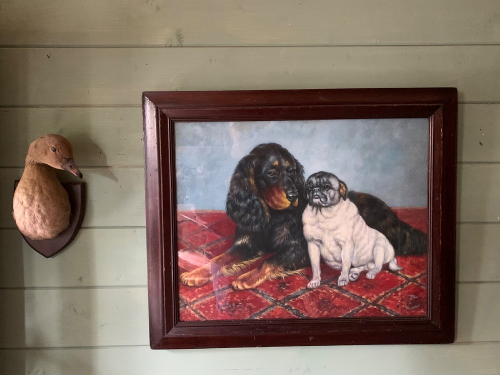 An oil painting on wooden panel depicting a black and tan spaniel resting next to a pug on a red patterned carpet inside a dark wooden frame. View II