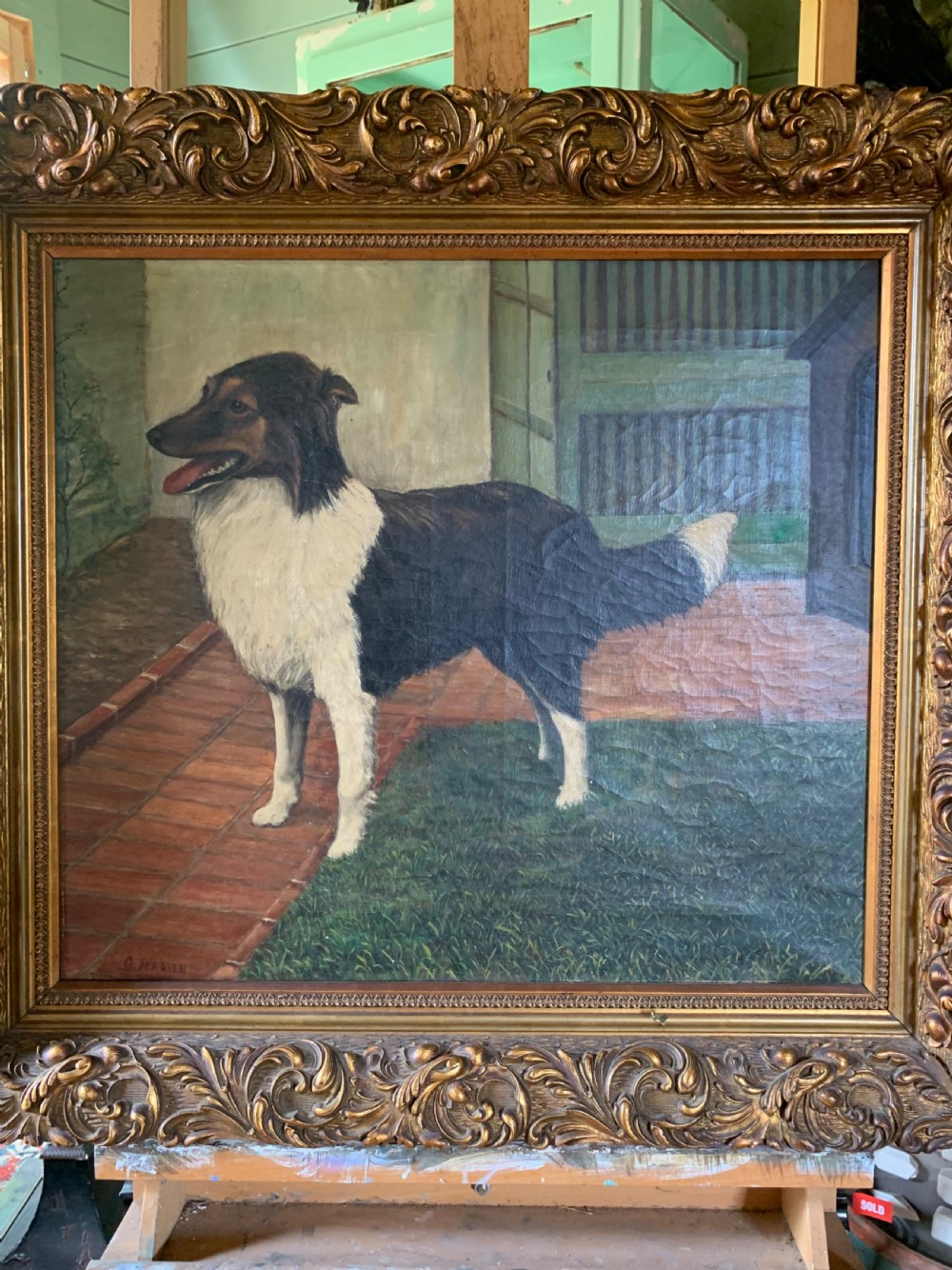 An antique oil painting depicting a black and white dog standing in a paved courtyard, encased in an ornate gold leaf frame. View III