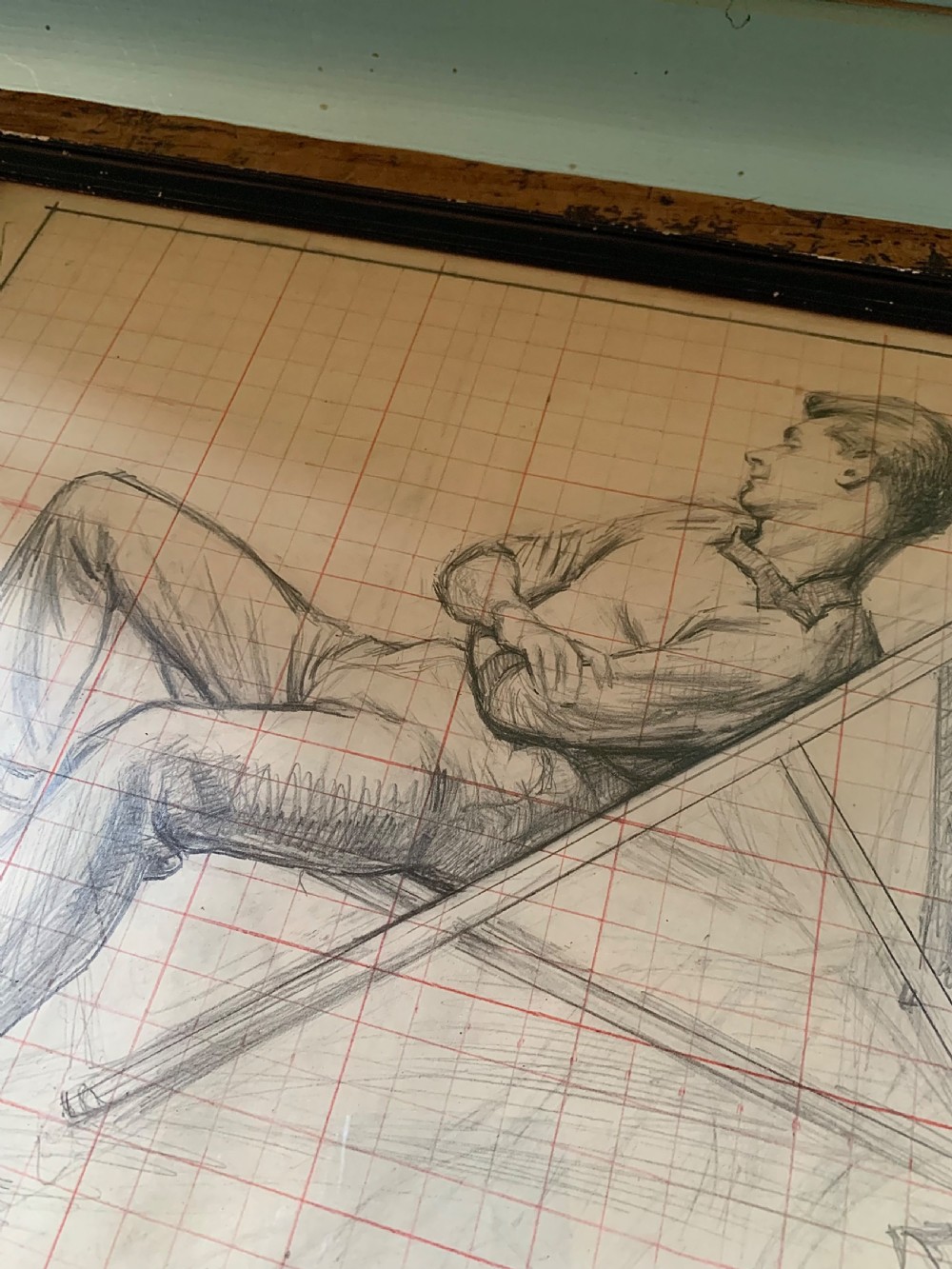 A framed monochrome pencil sketch on gridded paper showing a reclined male figure with arms crossed in a simple black frame. View V