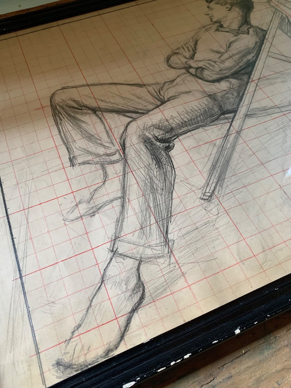 A framed monochrome pencil sketch on gridded paper showing a reclined male figure with arms crossed in a simple black frame. View VI