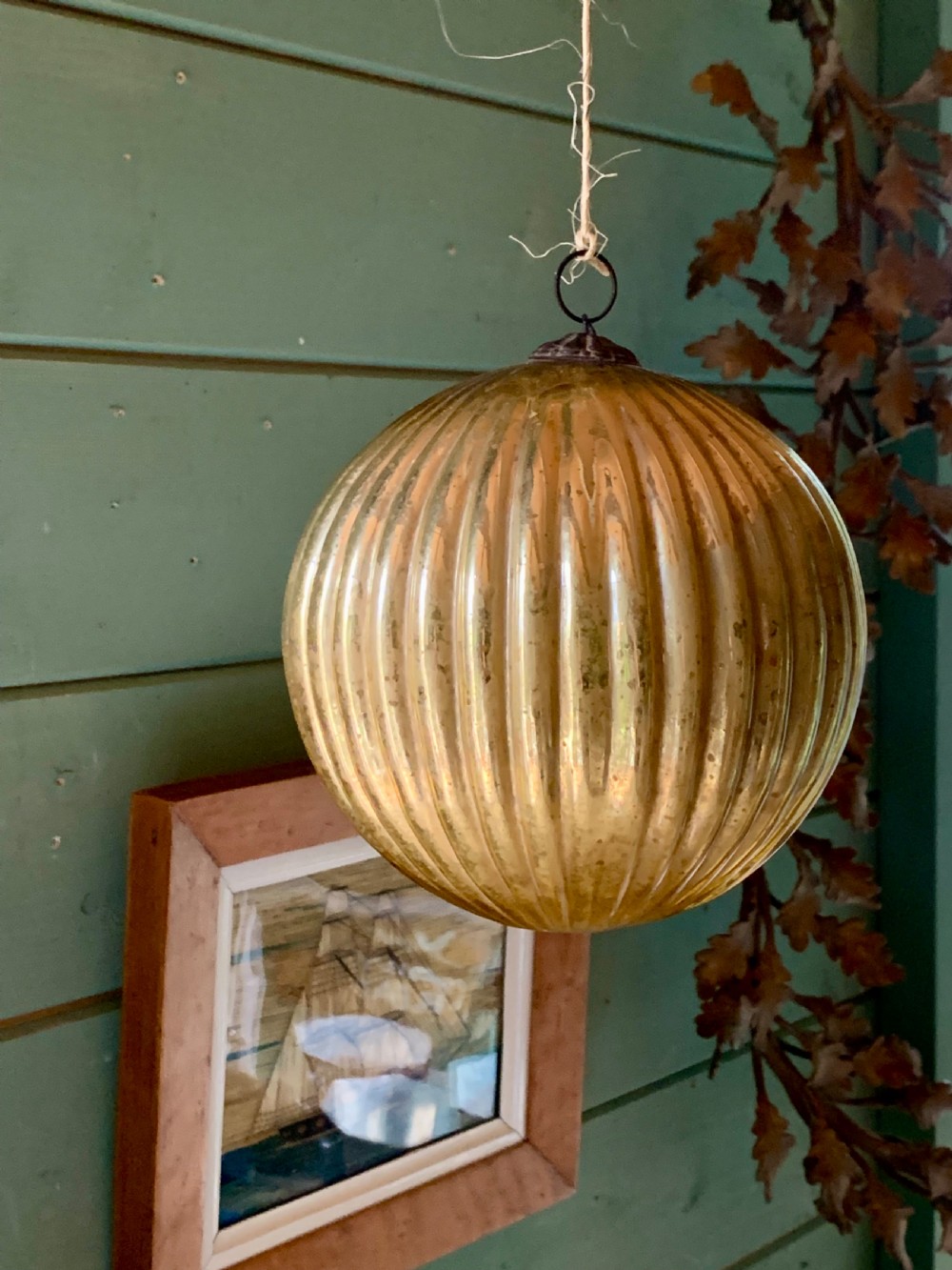 A spherical ribbed mercury glass kugel ornament displaying a silvered aged gold finish and top metal hanging loop. View II