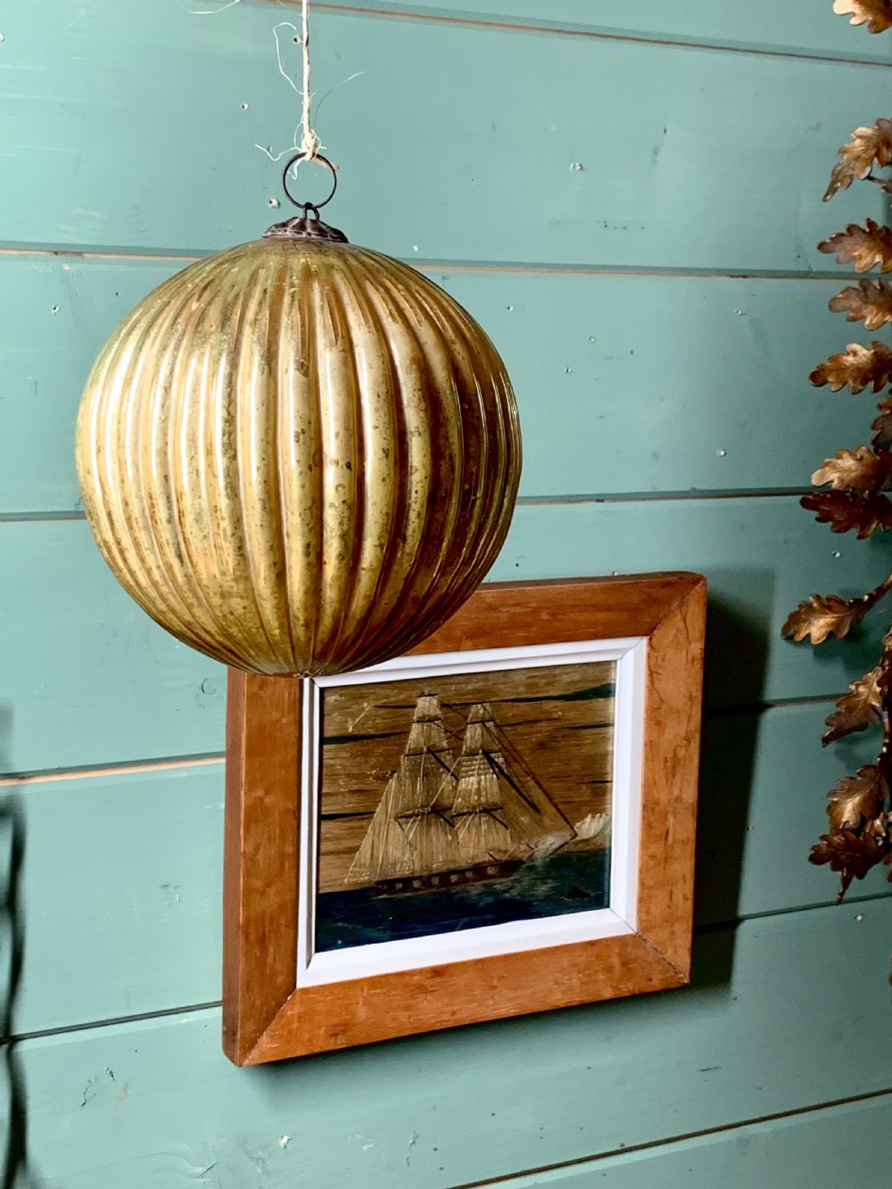 A spherical ribbed mercury glass kugel ornament displaying a silvered aged gold finish and top metal hanging loop. View IV