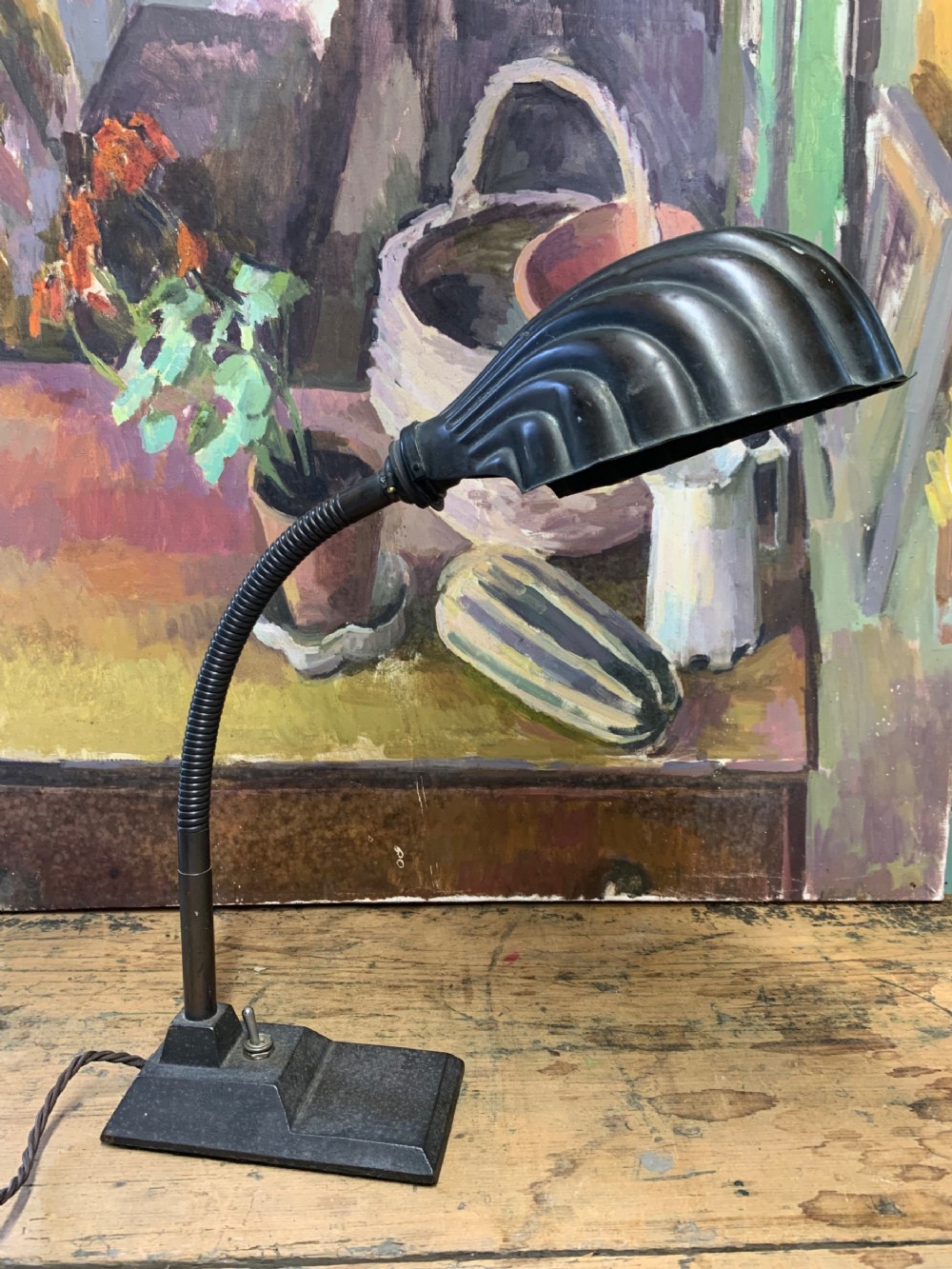 A 1930s black metal gooseneck desk lamp with a fluted clam shell shade and a rectangular stepped cast base featuring a toggle switch.